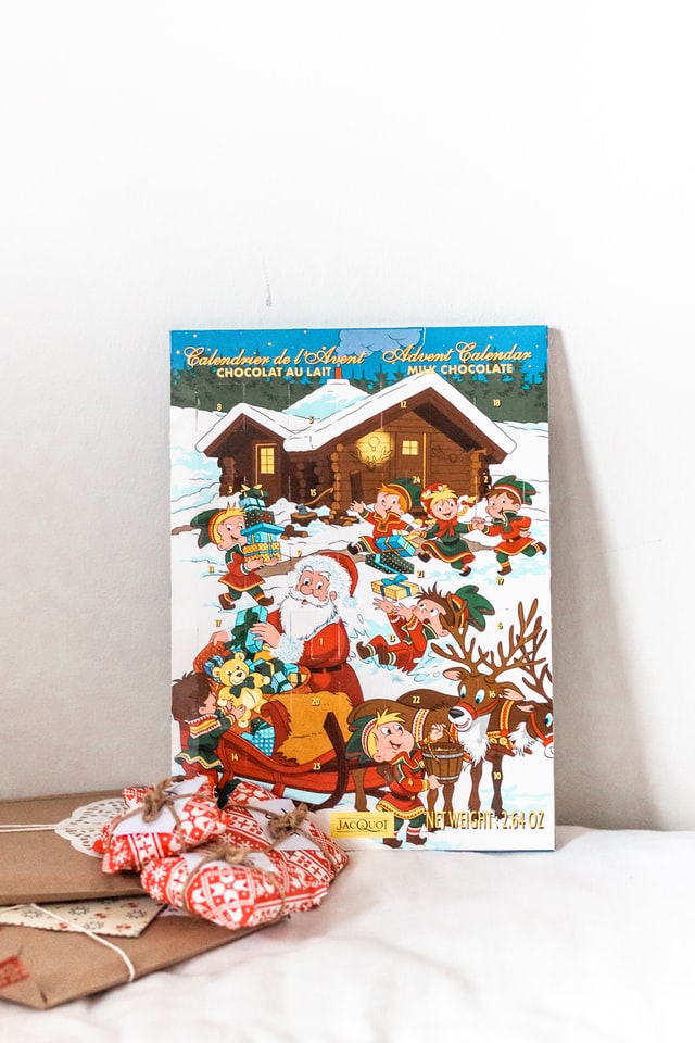 Ein bunter Adventskalender mit dem Weihnachtsmann und Wichteln darauf und Geschenke davor