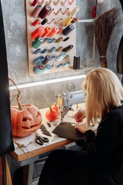 Eine Frau sitzt an einem Tisch mit verschiedenen Garnrollen und arbeitet an einer Nähmaschine