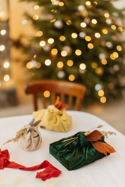 Auf einem Tisch liegen drei in Furoshiki eingewickelte Geschenke, im Hintergrund ein Weihnachtsbaum
