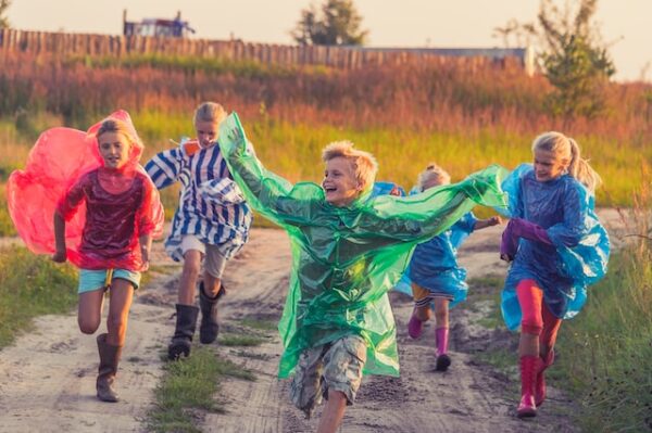 Kinder in bunten Regencapes rennen über einen Feldweg