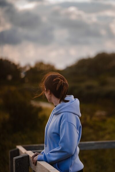 Frau mit blauem Kapuzenpullover steht an einem Geländer und schaut in die Ferne