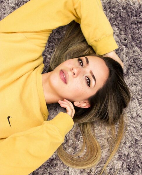 eine Frau trägt ein gelbes Sweatshirt und liegt auf einem flauschigen Teppich