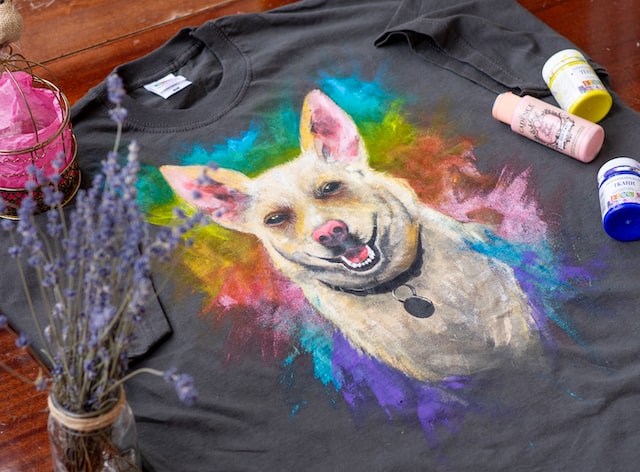 Ein T-Shirt mit aufgemaltem Hundeporträt, daneben Farben und Pinsel